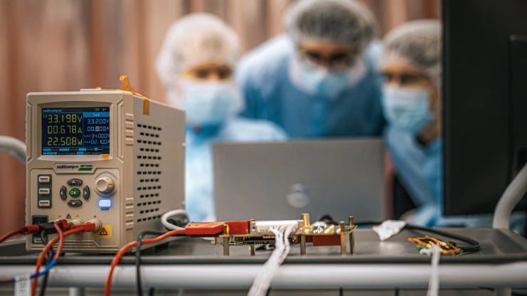 Test de câbles pour la production d'un satellite avec trois employés Aerospacelab floutés observant la scène en arrière plan.